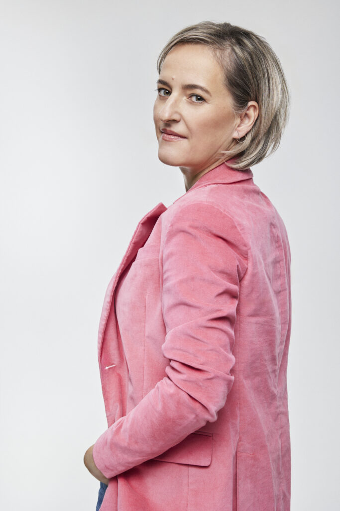 Basia standing with head facing us, in pink jacket