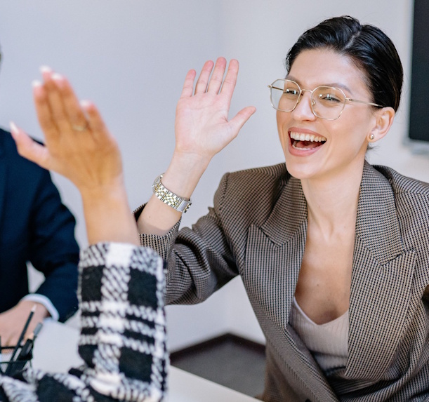 Photo of a cheerful woman in business-like attire, high-fiving a colleague